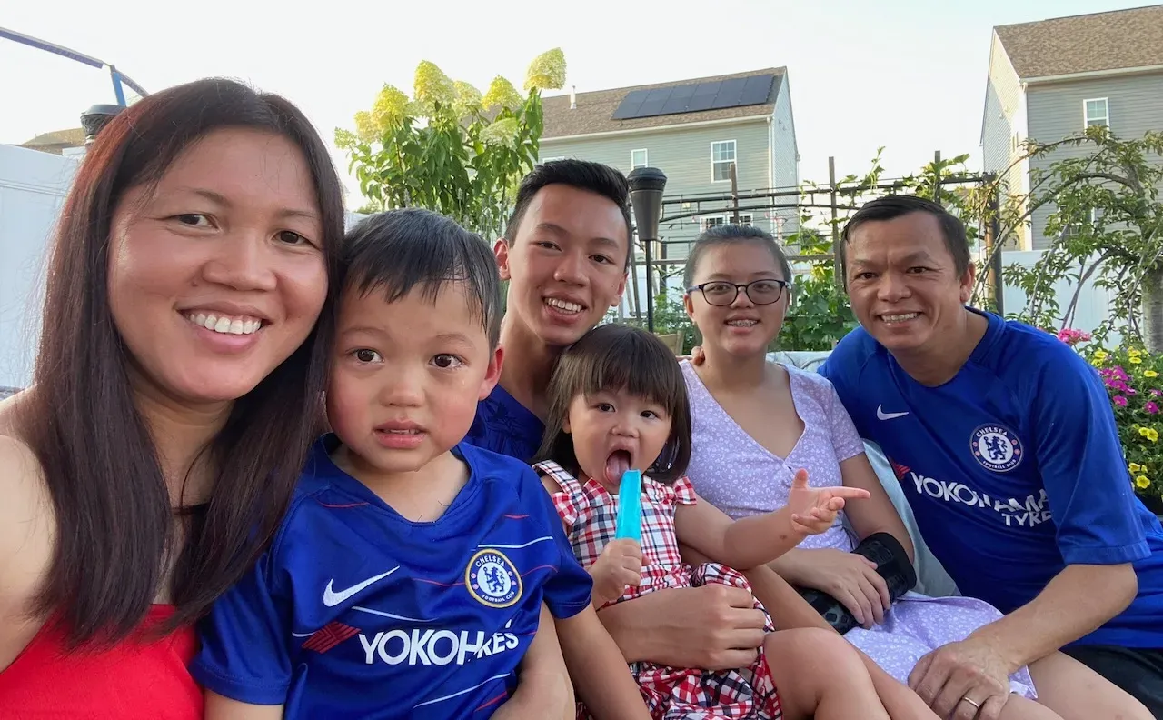 An Asian woman in her late thirties smiles on the left, and an Asian man smiles on the right. In between them are their four children, toddler to to teenage. They are in a backyard in what appears to be Maryland.